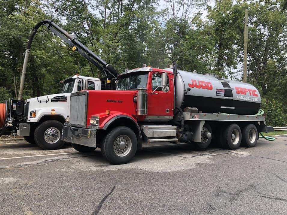 A Judd Septic Tank Cleaning truck is ready for septic tank service, parked beside another truck on a quiet road.